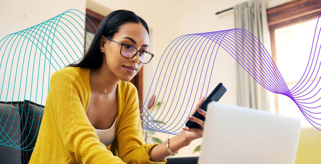 Woman in yellow sweater looking at her phone and laptop with gradient wavy lines in background