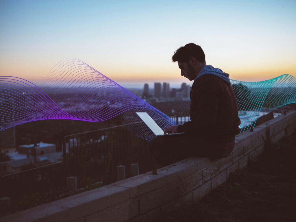 Man sitting on wall ledge working on his computer